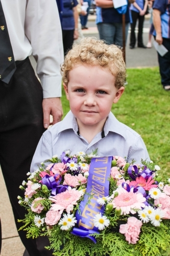 Young boy holding flower wreath with lest we forget sash for Anzac Day - Australian Stock Image