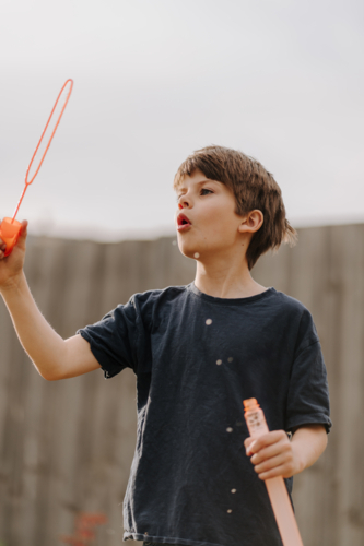 Young boy in black shirt blowing bubbles. - Australian Stock Image