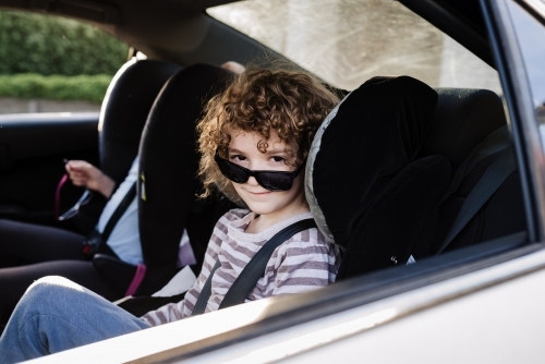 Young boy in the backseat of the family car with his sunglasses sitting down over his nose