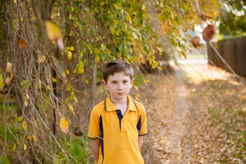 Young boy in yellow school uniform on leafy path