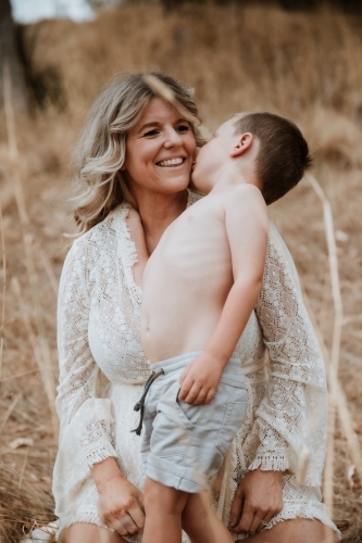 Young boy kissing his mother's cheek in a field of long grass - Australian Stock Image