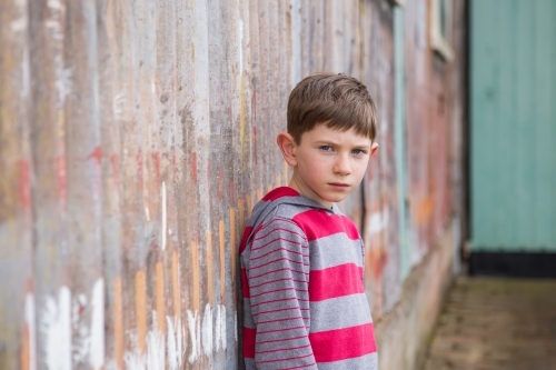 Young boy looking at camera in front of rusty iron wall