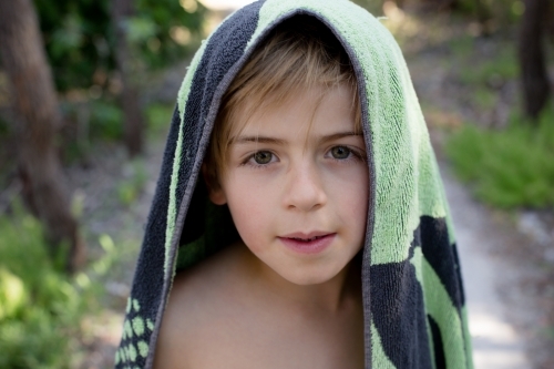 Young boy looking at camera with beach towel over his head - Australian Stock Image