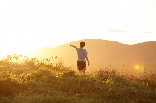 Young boy looking out to mountains at sunset - Australian Stock Image