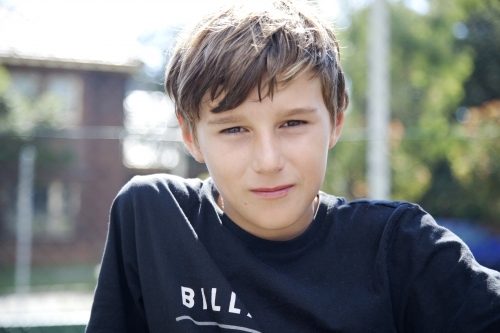 Young boy looking sitting outdoors on a sunny day - Australian Stock Image
