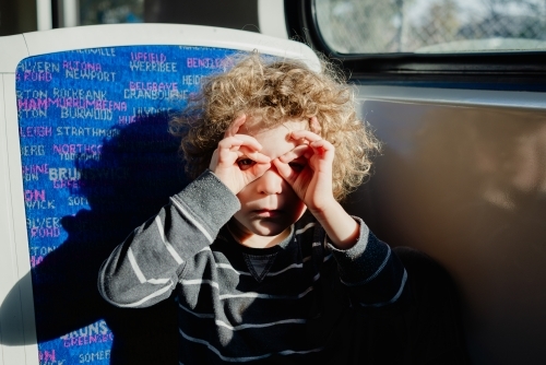 Young boy looking through hand glasses (finger glasses) sitting on a Melbourne suburban train - Australian Stock Image