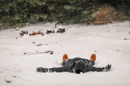 Young boy lying on his back in the snow with copy space - Australian Stock Image