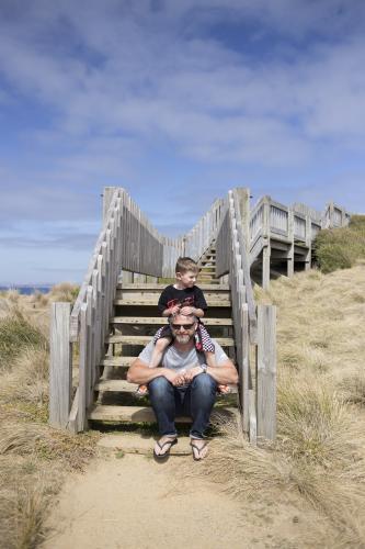 Young boy on Father's shoulders at the beach - Australian Stock Image
