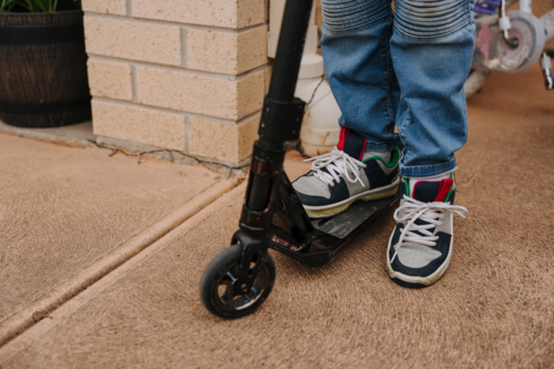 Young boy on his scooter outside of their house. - Australian Stock Image