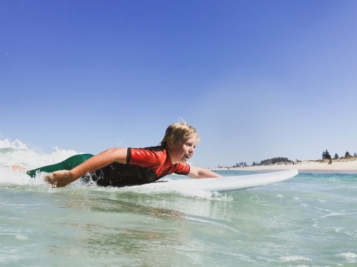Young boy paddling on surfboard going for wave