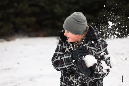Young boy playing in snowy winter wonderland snowball fight - Australian Stock Image