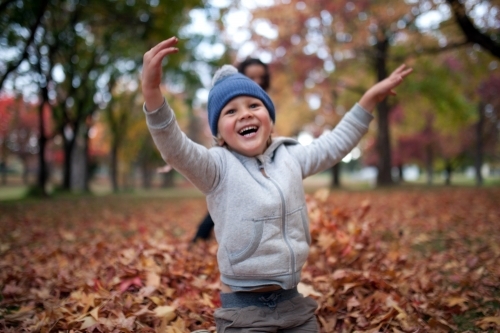Young boy playing outdoors among piles of autumn leaves - Australian Stock Image