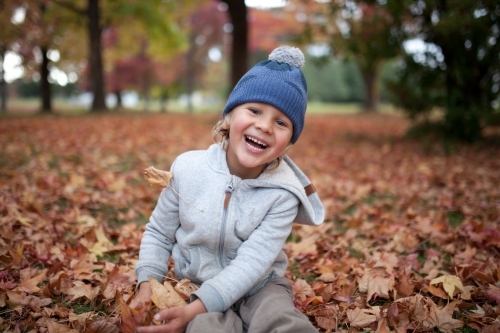 Young boy playing outdoors among piles of autumn leaves - Australian Stock Image