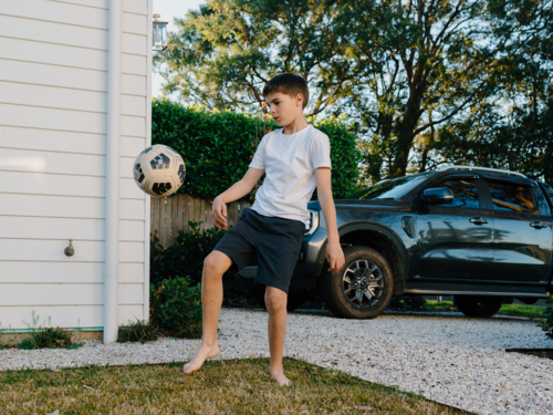 Young boy playing soccer outside in yard - Australian Stock Image
