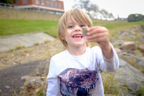Young boy playing with rocks by the water - Australian Stock Image