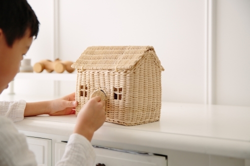 Young boy playing with small toy house with wooden car toy in the background - Australian Stock Image