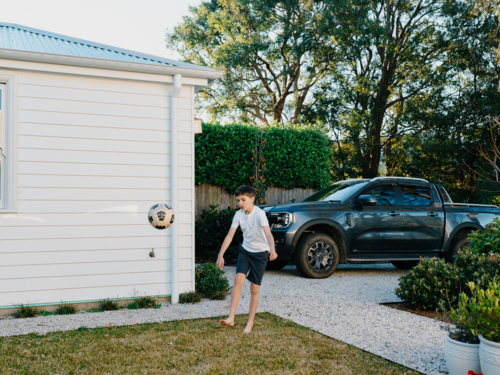 Young boy playing with soccer ball in suburban yard - Australian Stock Image