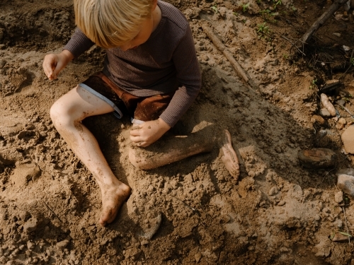 young boy playing with soil while sitting on the ground - Australian Stock Image