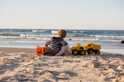 Young boy playing with toy trucks on the beach