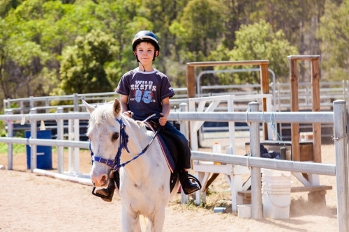 Young boy riding a white pony in dusty yards - Australian Stock Image