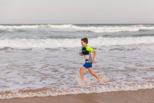Young boy running through water on beach in afternoon