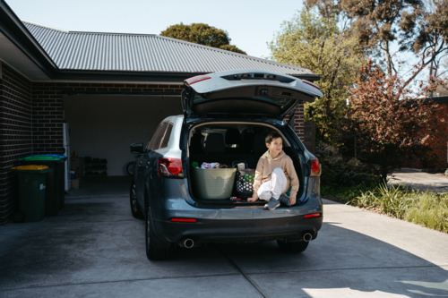 Young boy sitting in the boot of the car in driveway - Australian Stock Image
