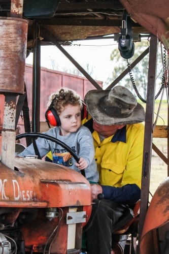 Young boy sitting on lap of farmer on tractor - Australian Stock Image