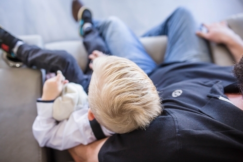 Young boy sitting on lounge in father's arm - Australian Stock Image