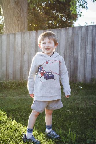 Young boy standing in afternoon sun beside timber fence - Australian Stock Image