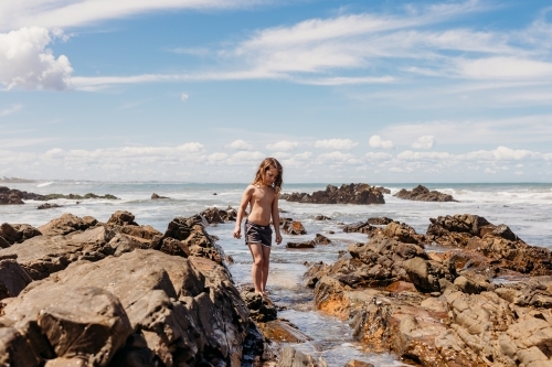 Young boy standing in ocean between rocks - Australian Stock Image