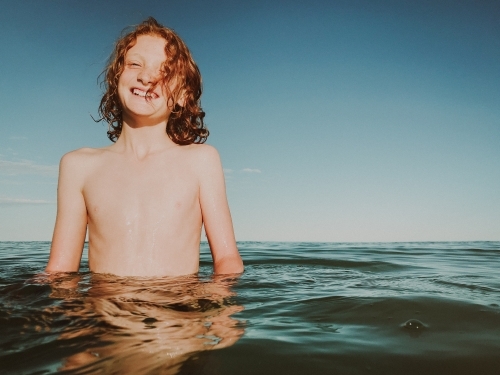 Young boy standing mid way in calm ocean - Australian Stock Image