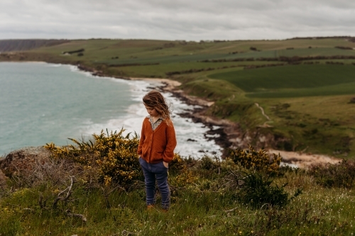 Young boy standing on cliff with green fields and ocean behind