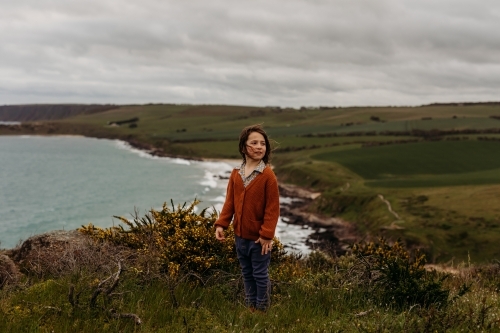 Young boy standing on cliff with ocean behind - Australian Stock Image