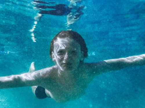 Young boy swimming underwater in blue ocean - Australian Stock Image