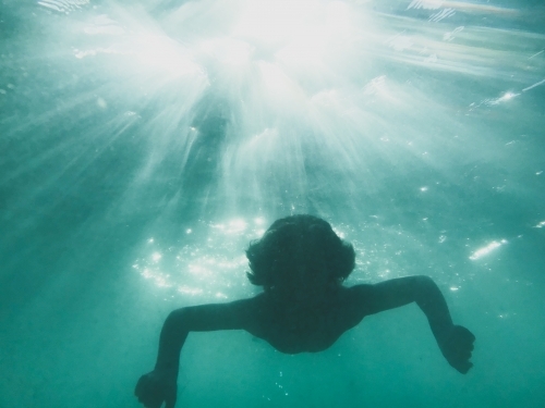 Young boy swimming underwater with sun beams through water