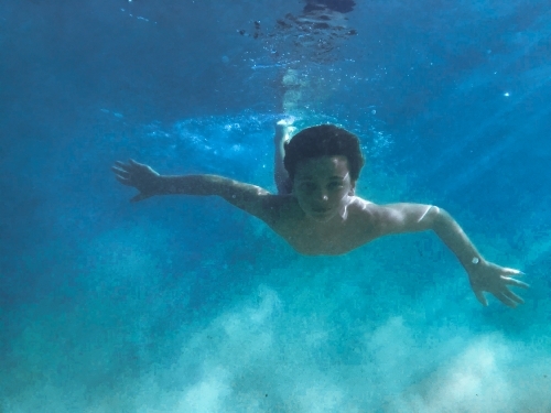 Young boy swimming underwater with sun beams through water - Australian Stock Image