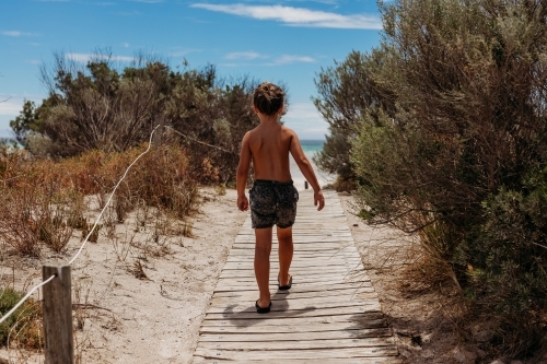 Young boy walking down a path to the beach