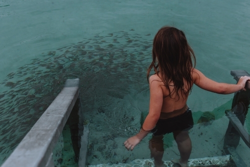 Young boy walking into water with school of fish - Australian Stock Image