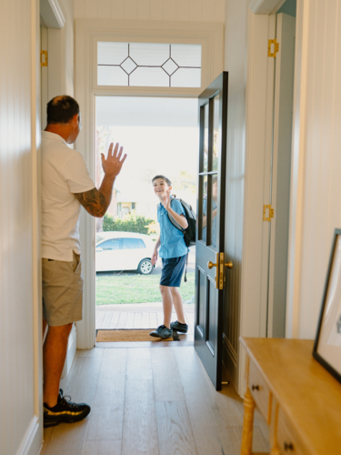 Young boy waving his hand goodbye to his dad at the doorway. - Australian Stock Image