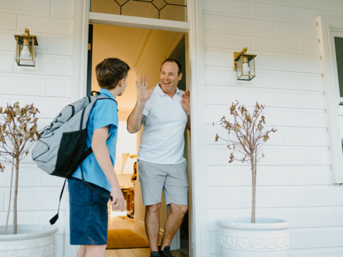 Young boy waving his hand goodbye to his dad at the doorway. - Australian Stock Image