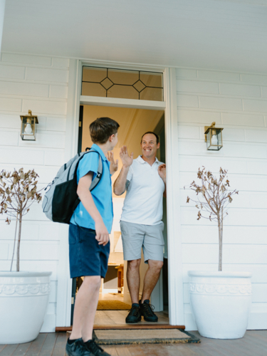 Young boy waving his hand goodbye to his dad at the doorway. - Australian Stock Image