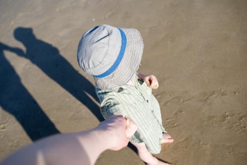 Young boy wearing a hat at the beach and holding hands seen from adult's POV