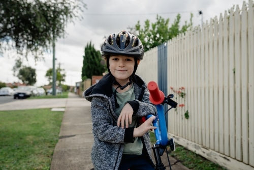 Young boy wearing bike helmet poses for a portrait on his bicycle; cycling around his neighbourhood - Australian Stock Image