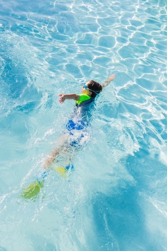 Young boy wearing googles and flippers swimming in pool - Australian Stock Image