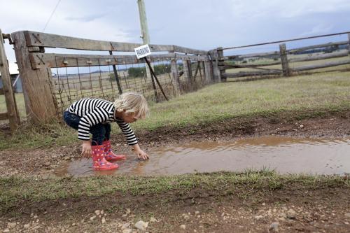 Young boy wearing gumboots playing in muddy puddle
