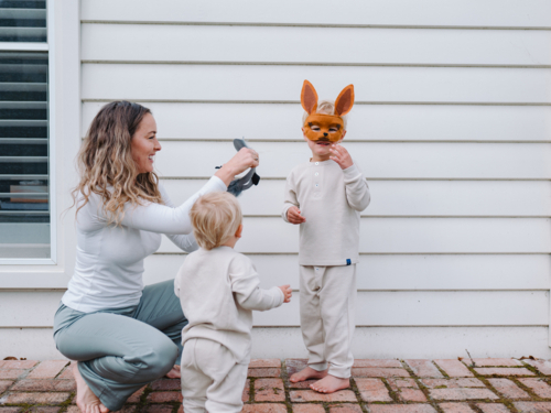 Young boy wearing kangaroo mask while mum crouching and holding koala mask for toddler brother - Australian Stock Image