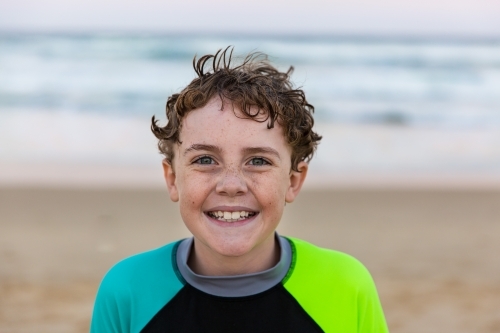 Young boy with freckles and curly hair smiling happy at beach - Australian Stock Image