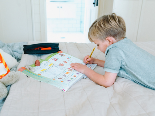 Young boy working on his workbook on the bed - Australian Stock Image