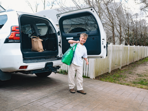 Young boys carrying green shopping bag out of car boot - Australian Stock Image
