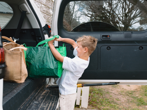 Young boys carrying green shopping bags out of car boot - Australian Stock Image